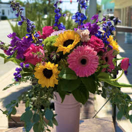 Bright mixed bouquet with sunflowers, pink gerberas, and purple blooms in a vase