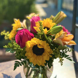Bouquet of pink roses, yellow sunflowers, and orange lilies in a glass vase