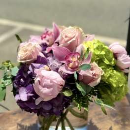 Pink roses and orchids arranged with purple hydrangeas in a glass vase