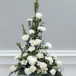 Tall white arrangement of roses, daisies, and carnations in a low container on a pedestal.