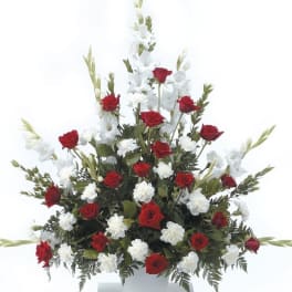 Tall fan-shaped arrangement of red roses and white flowers in a white urn container