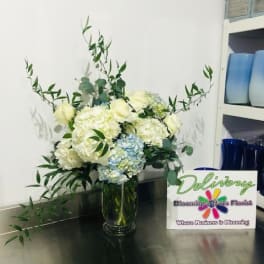 White and pale blue flowers in a glass vase with long greenery