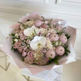 Large pastel bouquet with white orchids and pink roses wrapped in pink paper