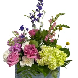 Mixed pink, purple, and green floral arrangement in a rectangular container