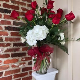 Red roses and white hydrangeas in a clear glass vase with a red ribbon