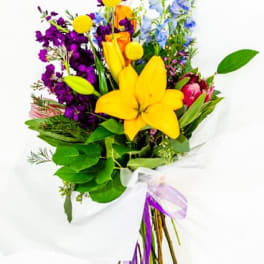Colorful bouquet with yellow lilies, purple flowers, and blue blooms wrapped in white paper