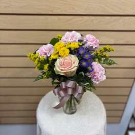 Bouquet of pink, yellow, and purple flowers in a glass vase with a ribbon