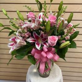 Pink roses and lilies arranged in a glass vase with a ribbon