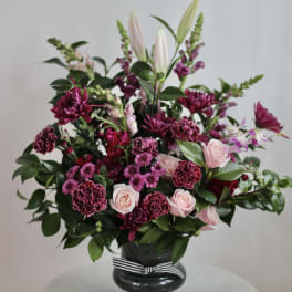 Pink and burgundy floral arrangement in a black vase