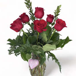 Red roses in a clear glass vase with a pink heart decoration