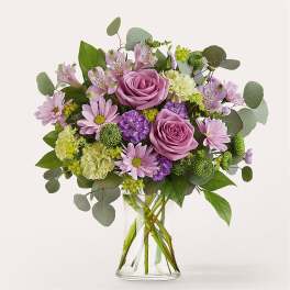 Lavender roses and mixed purple flowers in a clear glass vase
