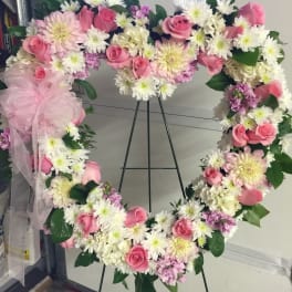 Heart-shaped floral wreath with pink roses and white daisies on an easel