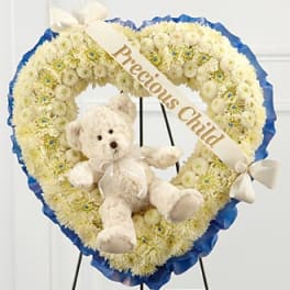 Heart-shaped white floral wreath with a teddy bear and ribbon banner