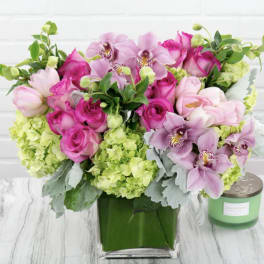 Pink roses and orchids arranged in a green vase with lime hydrangeas