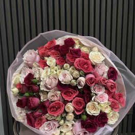 Large bouquet of pink, red, and cream roses wrapped in pale paper