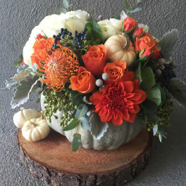 Orange and white floral arrangement in a pumpkin centerpiece with small pumpkins