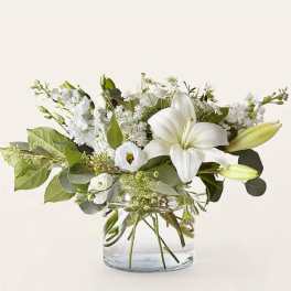 White lilies and mixed white flowers in a clear glass vase