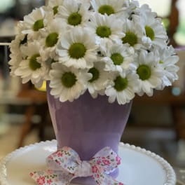 White daisies in a lavender vase with a floral ribbon bow