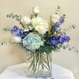 White roses and blue hydrangeas in a clear square vase