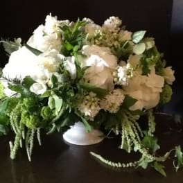 White floral arrangement in a low white vase with trailing greenery