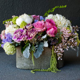 Mixed bouquet of pink roses, purple carnations, and white blooms in a concrete container