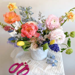 Colorful mixed flower arrangement in a white vase with pink scissors nearby