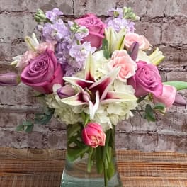 Bouquet of pink and lavender roses with white lilies in a glass vase