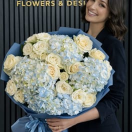 Large bouquet of cream roses and pale blue hydrangeas wrapped in blue paper