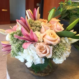 Bouquet of pink roses, lilies, and white hydrangeas in a glass bowl vase