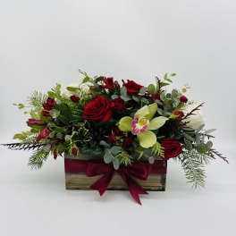 Low rectangular arrangement of red roses, white blooms, and green orchids in a wooden box with a red bow