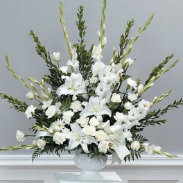 Tall all-white arrangement with lilies, roses, carnations, and gladiolus in a white urn.
