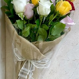 Wrapped bouquet of red, white, yellow, and pink roses in patterned paper with a white ribbon