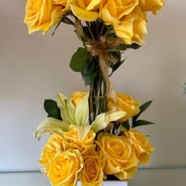 Tall arrangement of yellow roses and pale lilies in a white square vase