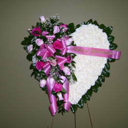 Heart-shaped floral tribute with pink roses and white flowers on a stand