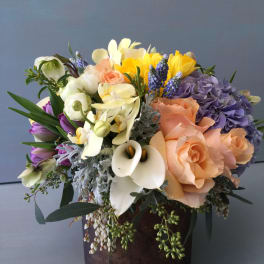 Mixed bouquet of peach, purple, white, and yellow flowers in a dark vase