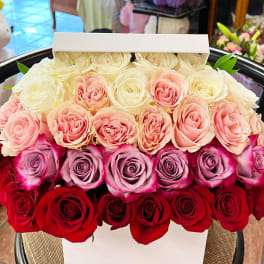 Boxed arrangement of roses in white, pink, lavender, and red