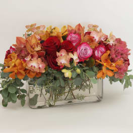 Mixed bouquet of roses and orchids in a clear rectangular vase