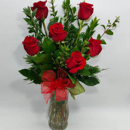 Red roses arranged in a clear glass vase with a red ribbon