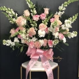 Large pink and white floral arrangement in a silver vase with a pink ribbon