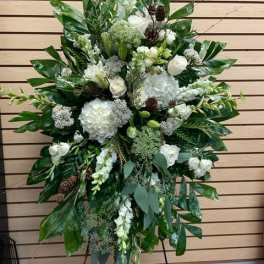 Large white floral standing spray with greenery and pinecones on an easel