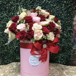 Pink hatbox arrangement of red and blush roses with a red ribbon