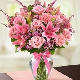 Pink bouquet of lilies, roses, and carnations in a glass vase with a ribbon