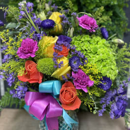 Colorful bouquet of roses, carnations, and purple blooms in a patterned vase