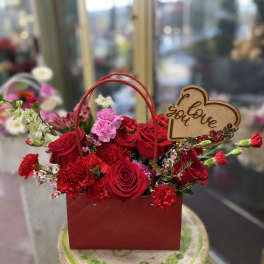 Red rose and carnation arrangement in a red handled gift box with a love sign