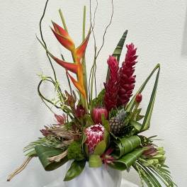 Tropical floral arrangement with red and orange blooms in a white vase