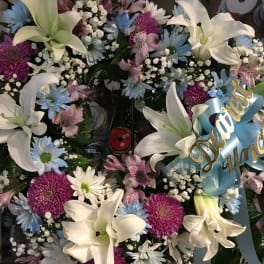 Floral wreath with white lilies, purple and blue daisies, and a blue ribbon