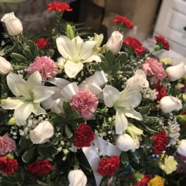 White lilies, roses, and red carnations in a ribboned bouquet