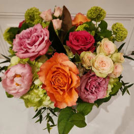 Mixed bouquet of orange, pink, and peach roses with pink peonies in a compact arrangement