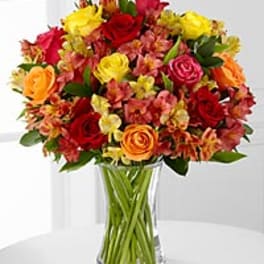 Mixed bouquet of red, yellow, and orange flowers in a clear glass vase