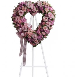 Heart-shaped floral wreath of pink roses and purple flowers on a white stand